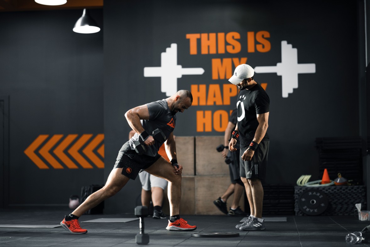 Coach sportif indépendant accompagnant un client pendant un exercice aux haltères, en salle de sport
